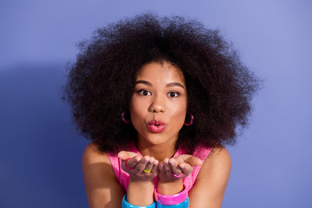 Smiling young woman with curly hair makes a blowing kiss gesture in a colorful retro style on a...