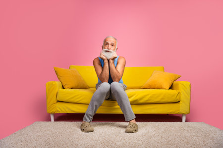 Elderly man with a beard seated on a colorful sofa in a cheerful home settingの写真素材