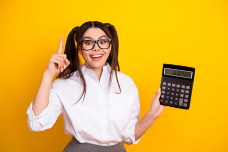 Young woman holding a calculator against a yellow background, showcasing educational and professional enthusiasm with youthful energyの写真素材