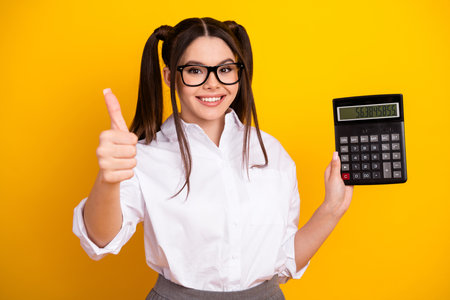 Cheerful student holding a large calculator, giving a thumbs up sign, wearing casual white shirt and stylish glassesの写真素材