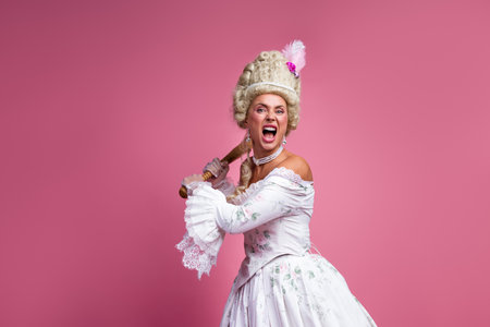 Stylish Woman in a Historical Gown Holding a Baseball Bat on a Pink Backdrop Expressing Passionate...