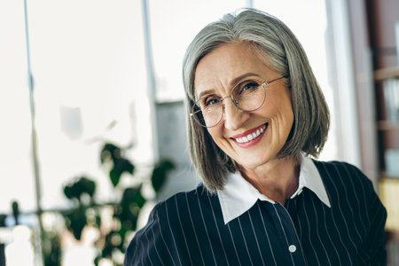 Confident mature businesswoman in elegant attire smiling in a professional workspace setting with...