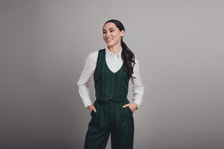 Stunning Young Businesswoman in Elegant Green Waistcoat Against Grey Background Smiling Brightlyの写真素材