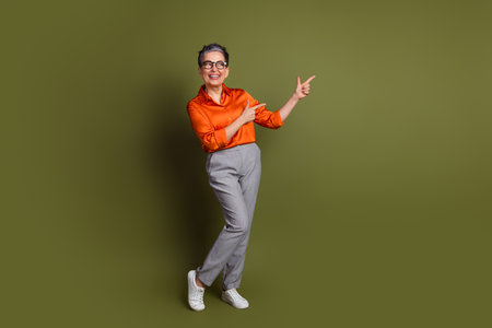 Stylish senior woman in vibrant outfit standing confidently against green background, energetically gesturing with a cheerful smileの写真素材