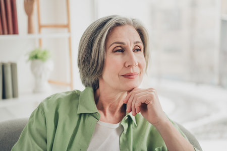 Portrait of a mature woman sitting indoors, reflecting peacefully and embracing a sense of comfort, leisure, and contentmentの写真素材