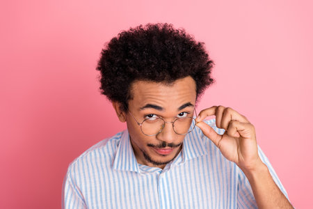 Young stylish man adjusting glasses on pink background demonstrating confident and trendy business style with eleganceの写真素材