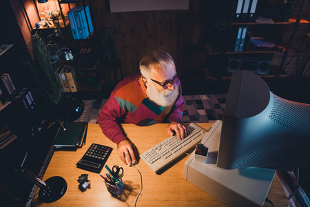 Elderly man working on computer in a cozy office space with focus on technology and creativity...