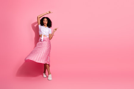 Joyful young woman in stylish pink attire dancing against a colorful background expressing fun and fashionの写真素材