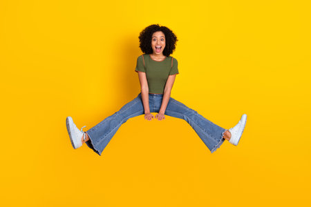 Young cheerful woman jumping excitedly with joy against a vibrant yellow background, dressed...
