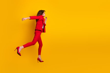 Confident young woman in a red suit gracefully posing against a vibrant yellow background, expressing elegance and fashion.の写真素材