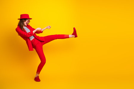 Charming young woman in a red suit joyfully posing against a vibrant yellow background, exuding fun, style, and energyの写真素材