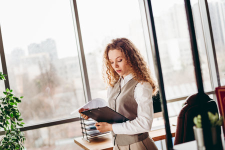 Confident Businesswoman in Modern Office Reading Documents by the Windowの写真素材