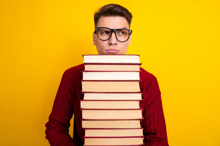 Young Male Student Holding Heavy book Against a Bright Yellow Background