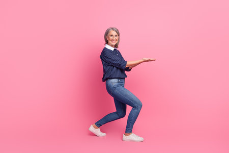 Mature woman gesturing with joy against a stylish pink backdrop, embodying confidence, elegance, and modern lifestyle dynamicsの写真素材
