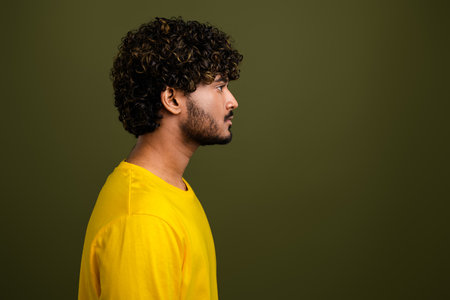 Profile portrait of a young man in a yellow shirt against a green background showcasing curly hair and casual styleの写真素材