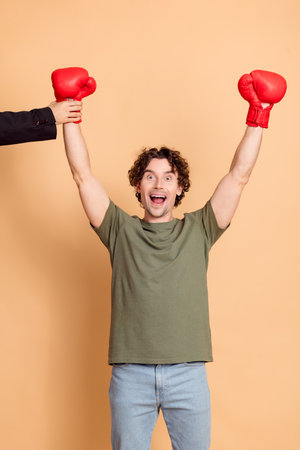 Excited young man with red boxing gloves celebrates success against beige background, conveying...