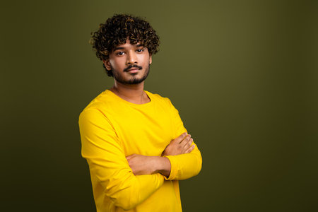Portrait of a confident young man in a yellow shirt with curly hair posing against a green backgroundの写真素材
