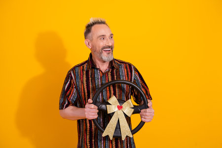 Cheerful man holding a decorated steering wheel on a vibrant yellow background, expressing joy