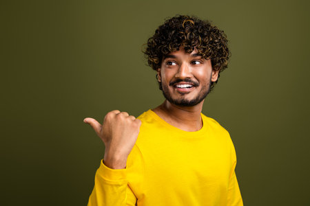 Portrait of a cheerful young man in stylish yellow shirt with curly hair, gesturing thumb up, against khaki backgroundの写真素材