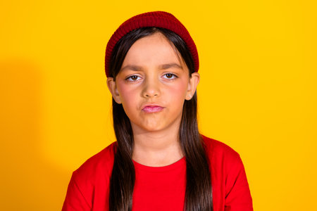 Portrait of a young brunette girl in casual red attire and a beanie set against a vibrant yellow...