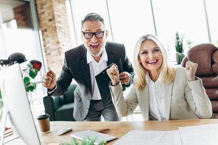 Senior colleagues celebrating success at the office with teamwork, positivity, and professional enthusiasmの写真素材