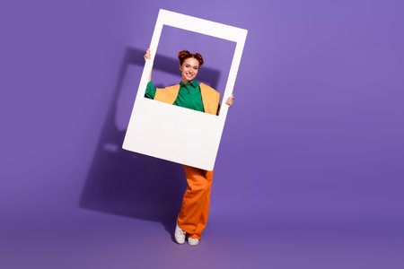 Happy woman holding a frame on bright purple background, showcasing a colorful and stylish outfit with a joyful expressionの写真素材