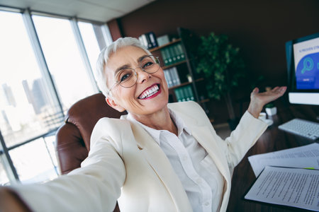 Confident senior businesswoman smiling in office workspace showcasing professional style and success.の写真素材