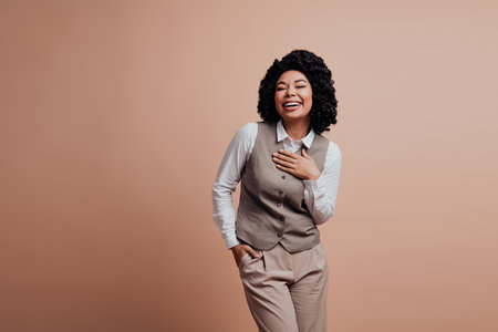 Confident young businesswoman in stylish beige formal attire smiles gracefully against a beige background in a casual poseの写真素材