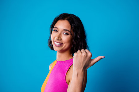 Young woman in vibrant pink top gesturing with cheerful expression against blue background, showcasing style and individualityの写真素材