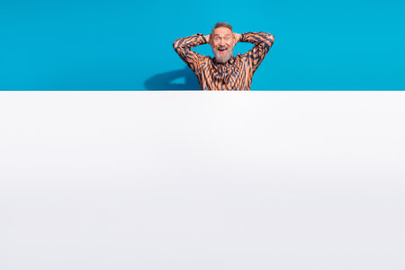 Stylish Mature Man Standing Against Blue Background with Hands Behind His Headの写真素材