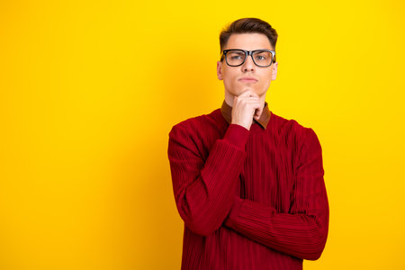 Young Confident Man in Red Sweater Against Vibrant Yellow Background Pondering Thoughtfullyの写真素材