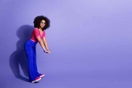 Cheerful woman in colorful retro fashion poses against vibrant purple background with playful expression for lifestyle conceptの写真素材