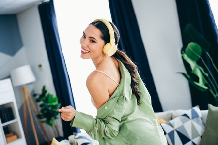 Adorable woman enjoying music with headphones at home in a stylish interior, expressing happiness...