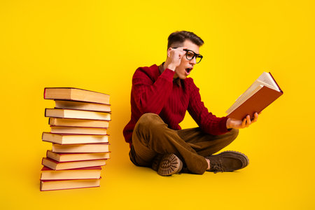 Intelligent student Young Handsome Man Reading Book in Casual Style Against a Bright Yellow Backgroundの写真素材