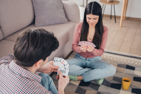 Young couple enjoying a casual card game indoors, sitting together on a rug in a cozy and bright living room in a relaxed atmosphereの写真素材