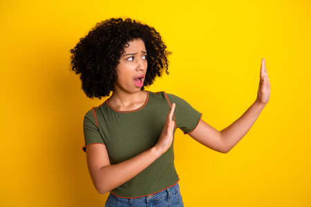Young woman in stylish casual outfit making expressive hand gesture against bold yellow wall...