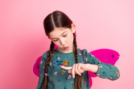 Adorable young girl with butterfly wings playfully pointing on a vibrant pink background showcasing her charming personalityの写真素材