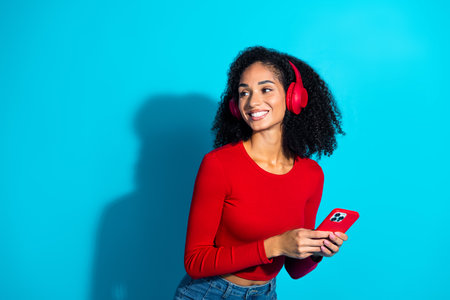 Happy young woman enjoying music on headphones with modern smartphone against a vibrant blue backgroundの写真素材