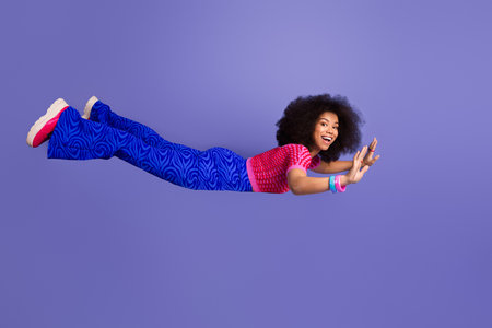 Young African American woman in vibrant retro fashion posing cheerfully against a purple background, hand extended playfullyの写真素材