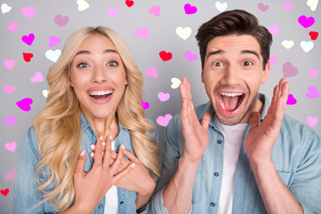 Photo of impressed adorable young people wear denim shirts rising arms hands chest smiling isolated grey color backgroundの写真素材