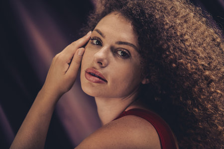 Portrait of a young woman with curly brown hair posing confidently against a stylish purple background in a studio settingの写真素材