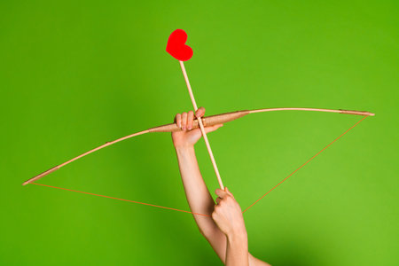 Hands holding a bow and arrow with red heart symbol on green background, love and Valentines Day concept.の写真素材