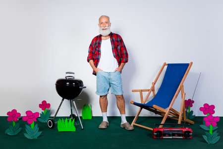 Mature man in casual attire enjoying a backyard scene with garden decor, barbecue grill, and deck chair against a bright background.の写真素材