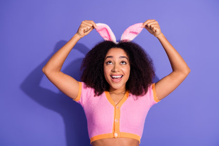 Young woman with afro hair wearing pink and orange top smiling playfully while posing against a vibrant purple background.の写真素材