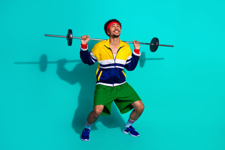 Young athletic man lifting a barbell in retro sportswear against a vibrant teal background, expressing an active and cheerful lifestyleの写真素材
