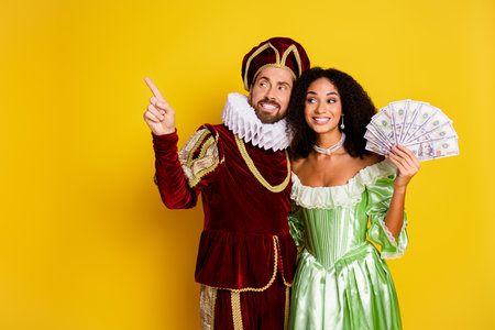 Elegant Couple in Period Costumes Holding Money Against a Bright Yellow Backgroundの写真素材