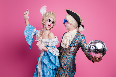 Joyful couple dressed in elegant 18th-century costumes enjoying a festive carnival theme party with...
