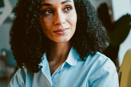A young woman with curly hair and a serene expression enjoys a moment of relaxation indoors in a stylish and natural setting.の写真素材