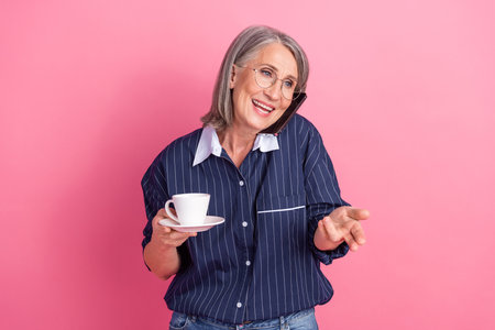 Mature woman enjoying a casual conversation while drinking coffee against a vibrant pink background