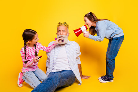 Amusing moment of a senior man with girls against a vibrant yellow background, portraying fun and family connectionの写真素材
